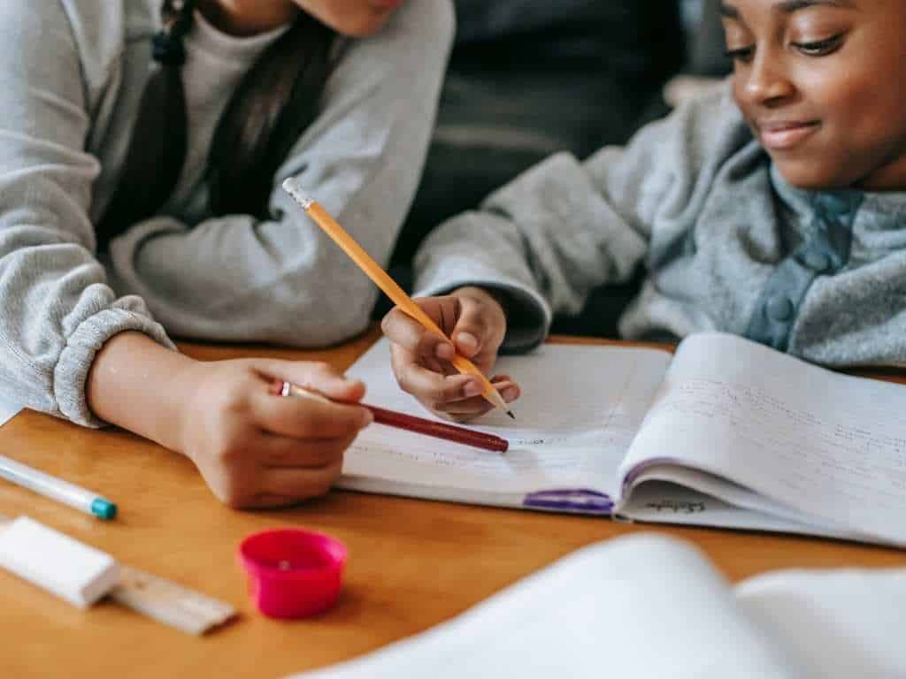Educación inicial: docente guiando a estudiante en ejercicios y tareas escolares Niña y adulto trabajando juntas en una mesa, escribiendo y resolviendo ejercicios en cuadernos, durante una actividad educativa personalizada.