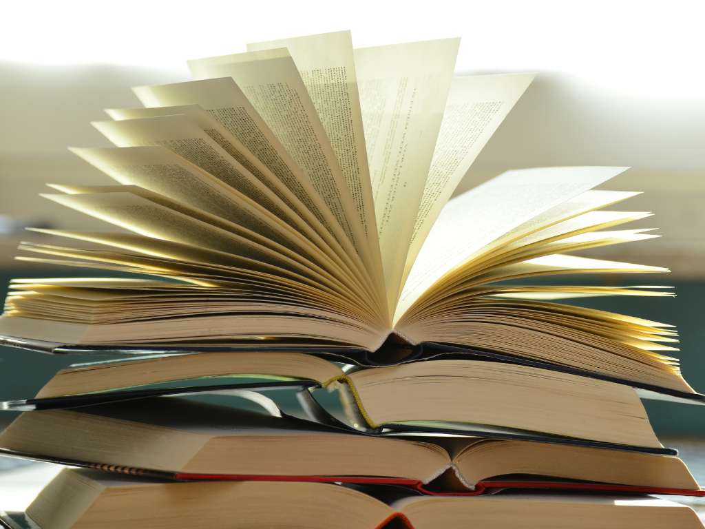 Libros para investigación académica: consulta de fuentes y ejemplos de temas para tesis Libros abiertos apilados, con páginas desplegadas, simbolizando investigación, consulta bibliográfica y búsqueda de información académica.