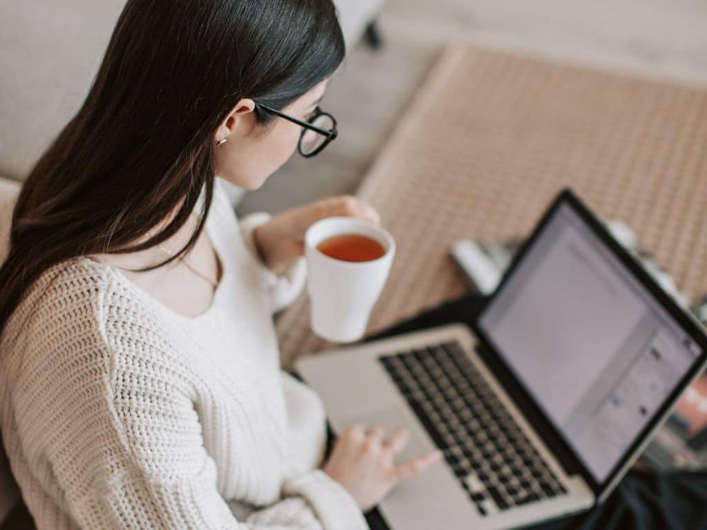 Revisión de repositorios de tesis para fundamentación académica Joven revisando trabajos académicos en laptop y tomando té mientras explora repositorios de tesis