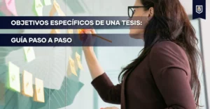 Portada con el texto "Objetivos específicos de una tesis: guía paso a paso" sobre una persona organizando notas adhesivas, representando la planificación de tareas concretas en la investigación