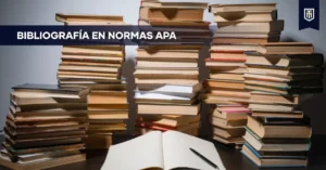 Mesa con cuaderno abierto y bolígrafo frente a grandes pilas de libros, con el texto “Bibliografía en Normas APA”, simbolizando la organización de referencias académicas según APA 7ª edición